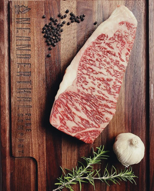 A raw Wagyu New York Steak on a cutting board.
